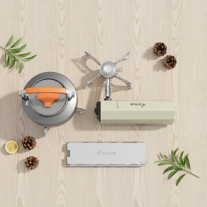 Portable folding cassette camping stove flat lay - cream white stove, 1.6L aluminum kettle with orange handle, and folding aluminum wind deflector